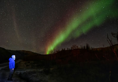 Side view of man standing against star field with aurora polaris at night