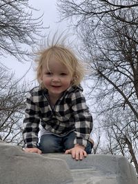 Cute smiling boy on rock against bare tree