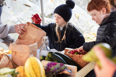 Girl buying red pepper bell while standing with family at market stall