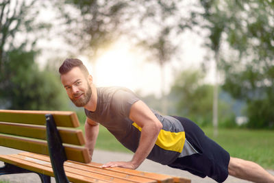 Portrait of smiling man doing push-ups on bench in park