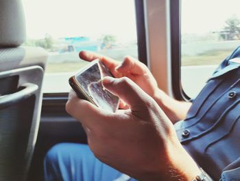 Midsection of man using smart phone in train