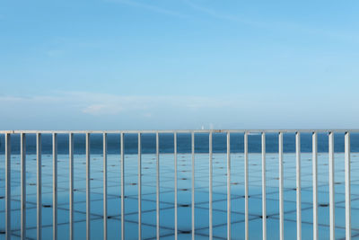 Wooden fence by sea against blue sky