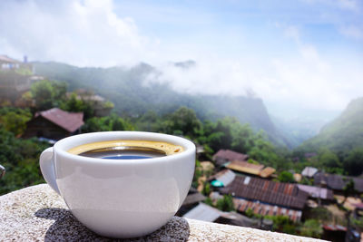Close-up of coffee cup on retaining wall against mountain range