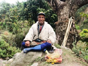 Portrait of man sitting on rock against trees