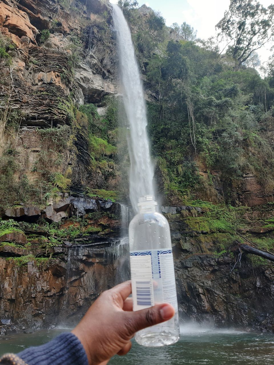 CROPPED IMAGE OF HAND HOLDING WATER FLOWING THROUGH WATERFALL