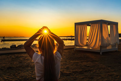 Rear view of woman standing at beach during sunset