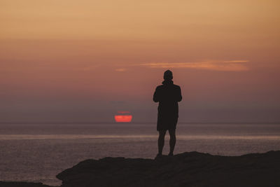 Young and watches sun rising in the distance as capture the moment on his phone.