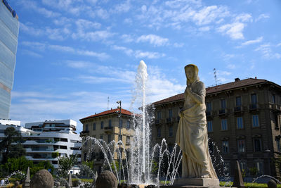 Statue by fountain against buildings against sky