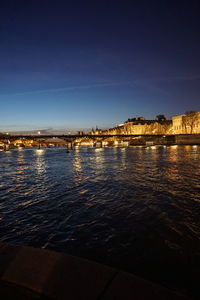 River by illuminated city against blue sky at night