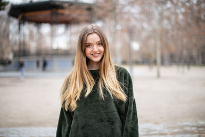 Portrait of smiling young woman with long hair standing in park during winter