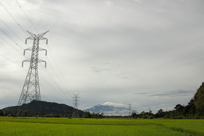 Low angle view of electricity pylon on field against sky