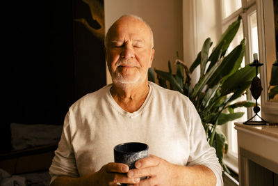 Senior man with eyes closed holding coffee cup at home