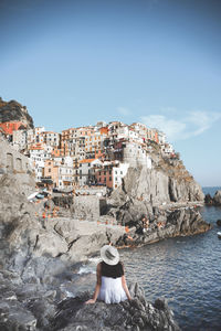 Rear view of woman sitting by sea on rock at cinque terre