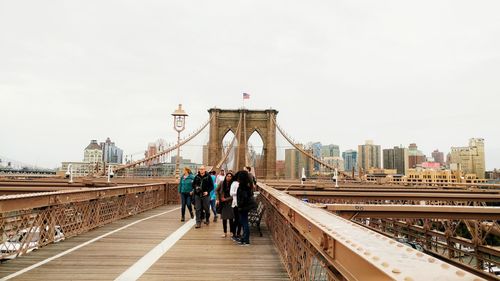 People on suspension bridge against sky in city