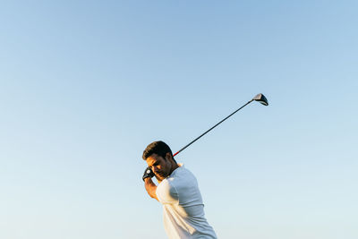 Professional male golf player preparing to hit ball with putter in green field while looking down on summer day