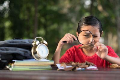 Boy looking through magnifying glass on table in park