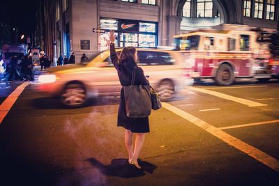 Rear view of woman hailing taxi on street at night