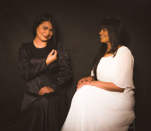 Portrait of smiling woman with friend against black background