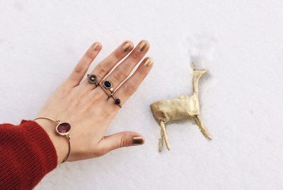 Cropped hand of woman wearing jewelry over statue in snow