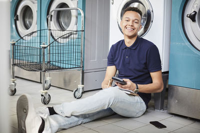 Portrait of smiling man holding calculator and studying while sitting besides washing machine