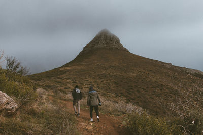 Rear view of hikers on mountain against sky during foggy weather