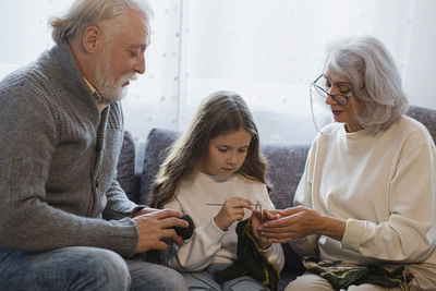 Grandparents teaching crocheting to granddaughter on couch