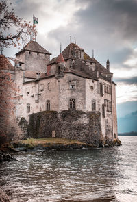 View of old building by river against cloudy sky