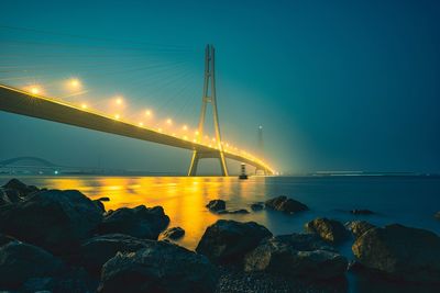 Illuminated bridge over sea against sky