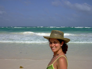 Portrait of happy young woman wearing hat on sunny day at beach against sky