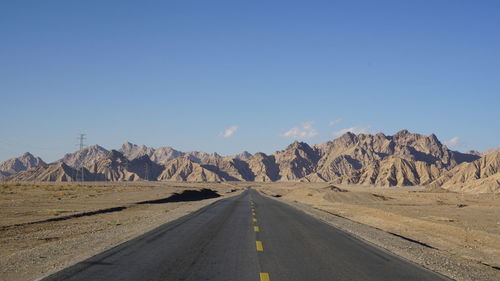 Empty road by mountains against clear blue sky