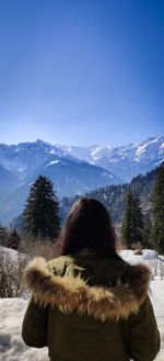 Rear view of woman standing on snowcapped mountain against sky