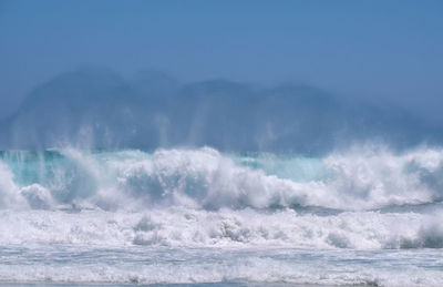 Waves splashing in sea against blue sky