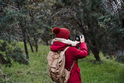 Rear view of woman photographing against trees in forest