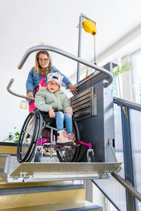 Mother and child living with cerebral palsy using wheelchair lift to access public building.