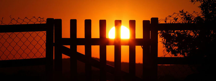 Silhouette fence against orange sky during sunset