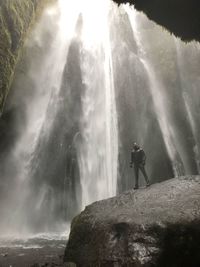 Hiker standing on rock formation against scenic waterfall at forest