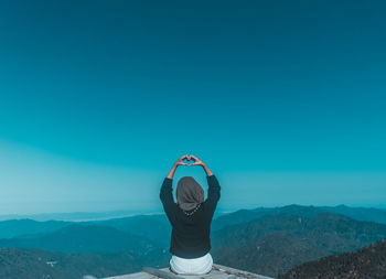 Rear view of woman showing heart shape while sitting at observation point