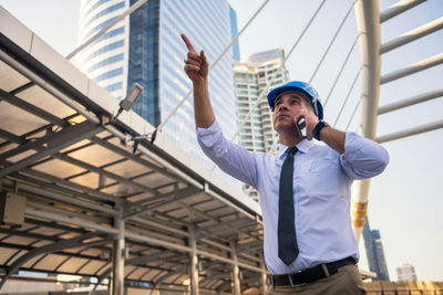 Low angle view of man pointing up while talking on smart phone