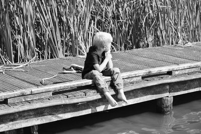 Full length of boy sitting on jetty against plants