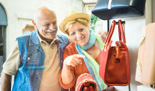 Senior woman pointing and showing man purse at retail display while standing outside store