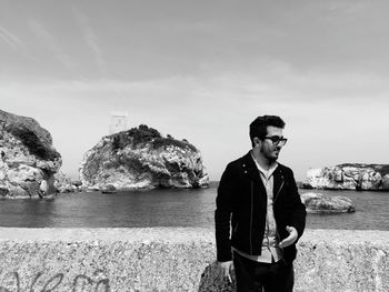 Young man standing by retaining wall against sea 