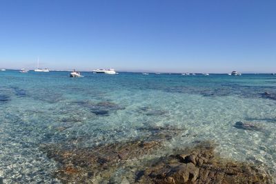 Boats in sea against clear blue sky