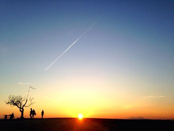 Silhouette tree against vapor trails in sky