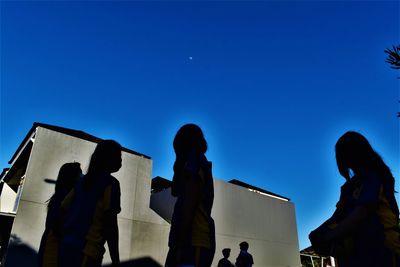 Low angle view of silhouette people against blue sky