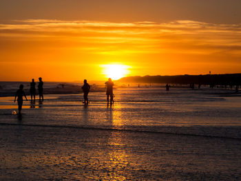 Silhouette people on beach against sky during sunset