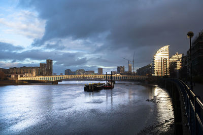 Bridge over river by buildings against sky at dusk