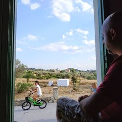 Man sitting by window against sky