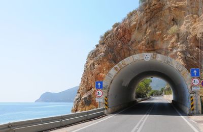 Road leading towards tunnel by sea on sunny day