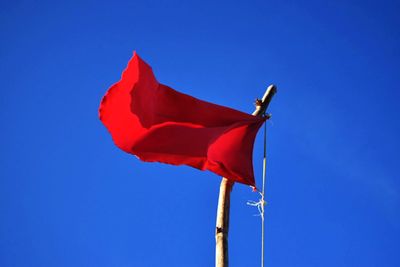 Low angle view of red flag against blue sky