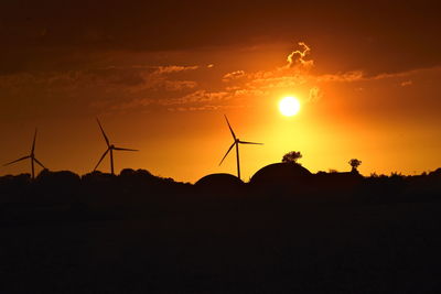 Silhouette wind turbines on field against sky at sunset